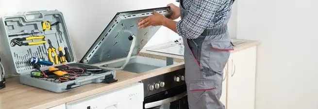 Cooktop repair technician lifting a built-in stovetop for service in Atlanta, GA