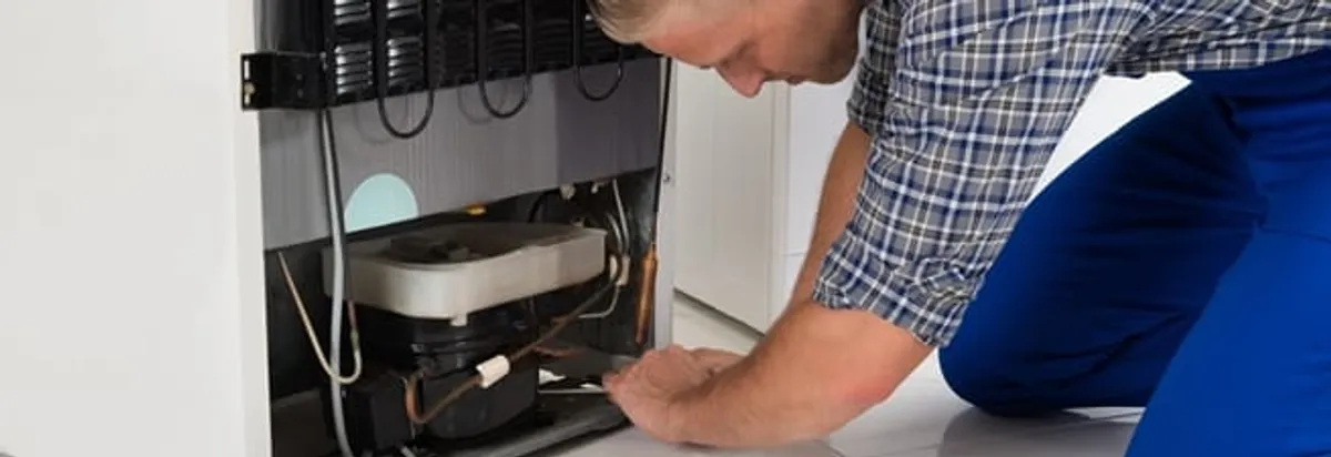 Refrigerator repair technician servicing the compressor and condenser area in Atlanta, GA