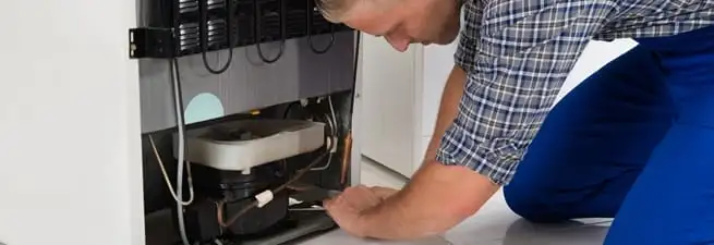 Refrigerator repair technician servicing the compressor and condenser area in Atlanta, GA