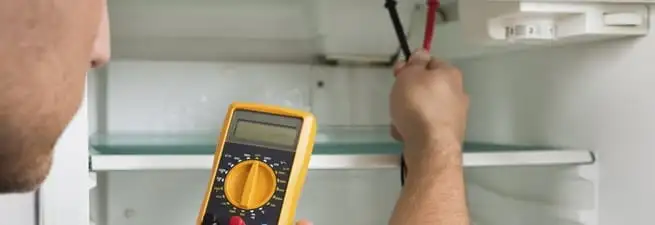 Refrigerator repair technician testing electrical components with a multimeter in Atlanta, GA