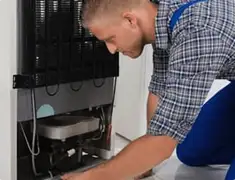 Refrigerator repair technician servicing the compressor and condenser area in Atlanta, GA